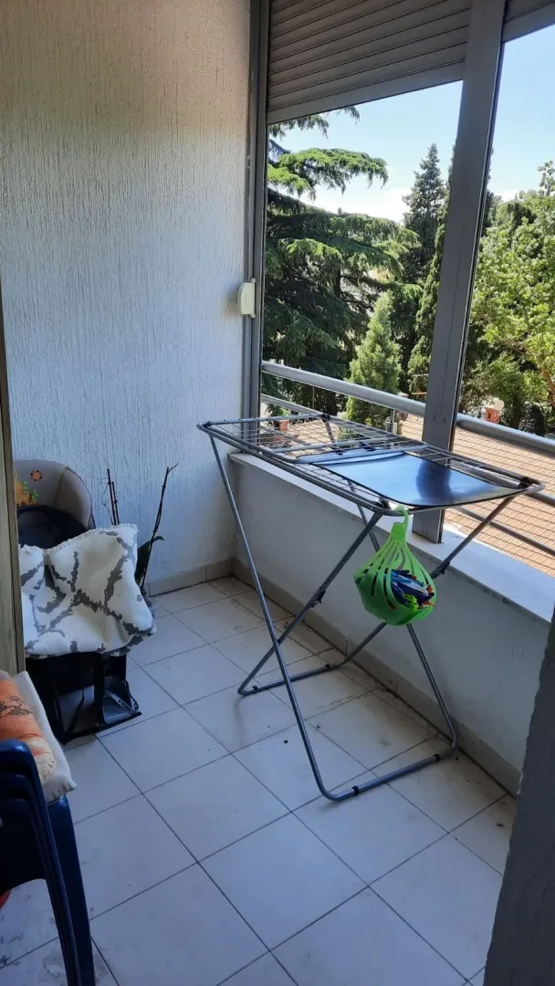 Balkon sa sušilicom za veš i pogledom na drveće.