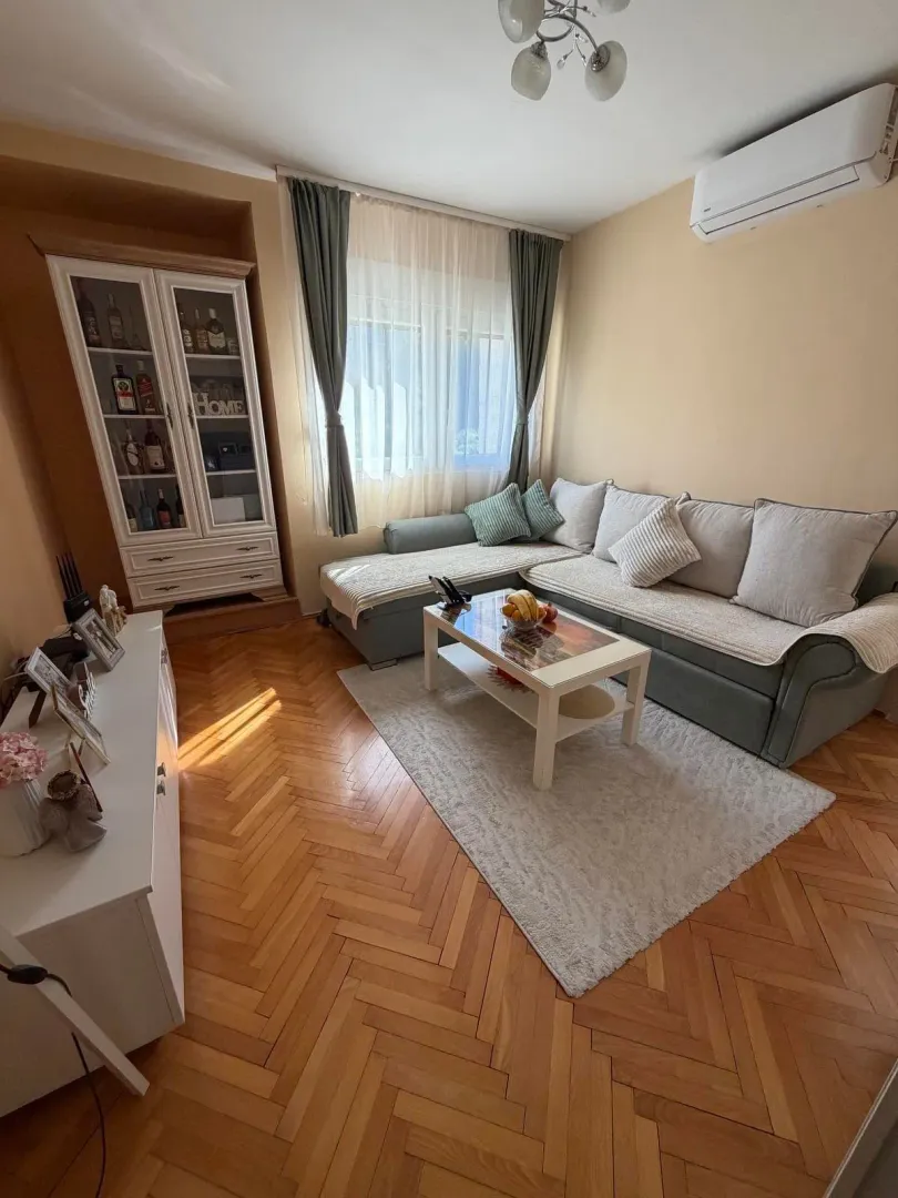 Dnevna soba sa garniturom, komodom i drvenim podom.