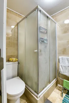 Kupatilo sa tuš kabinom i toaletom u bež pločicama. - image 19