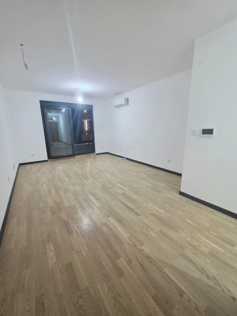 Prazna soba sa parketom i bijelim zidovima.