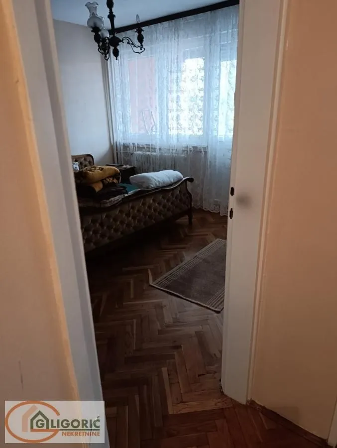 Pogled iz hodnika na nameštenu spavaću sobu sa drvenim podom.