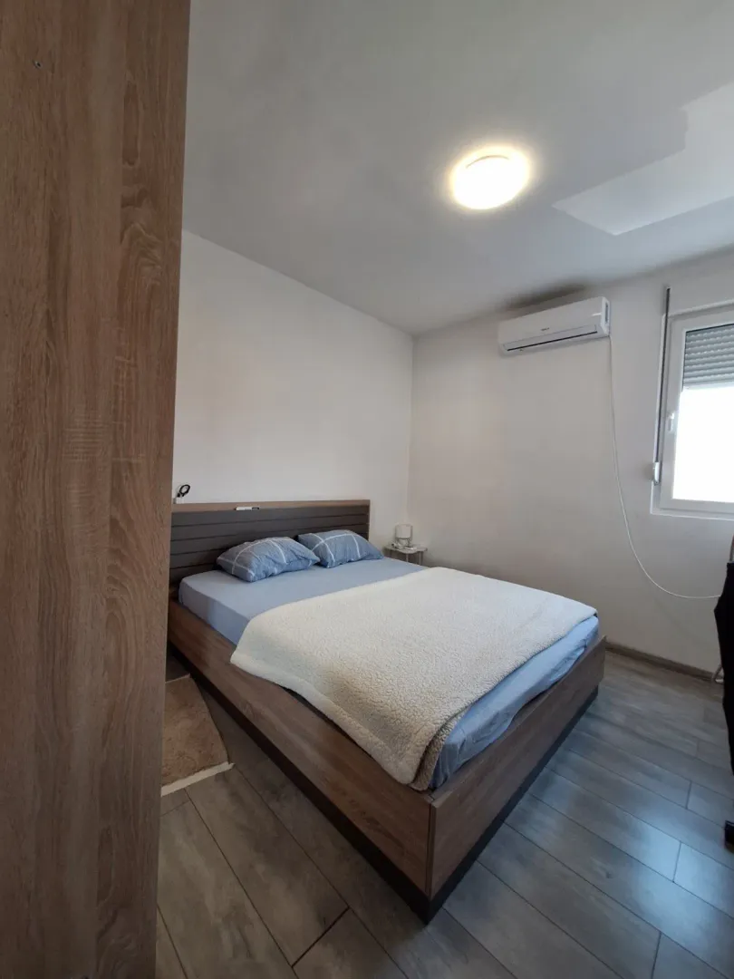 Manja spavaća soba sa bračnim krevetom, klima uređajem i prozorom.