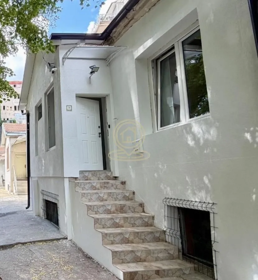 Spoljašnji izgled kuće sa ulaznim stepeništem i belom fasadom.