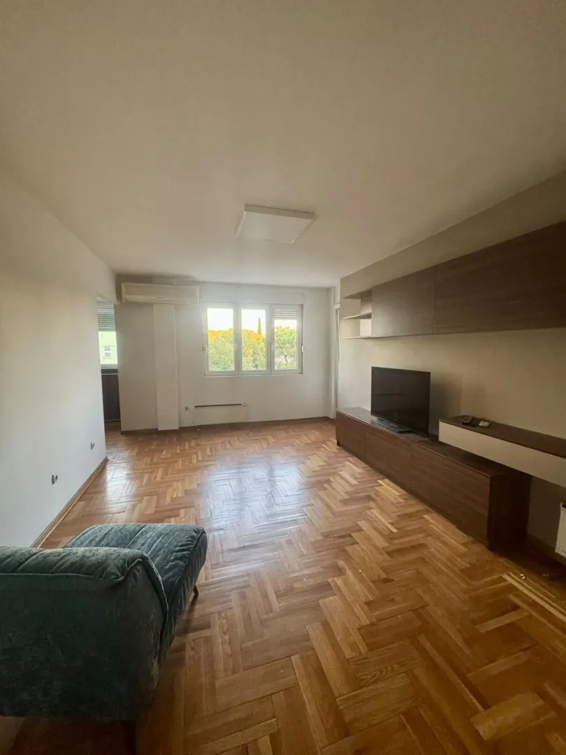 Living room with wooden parquet flooring, furniture, and a television.