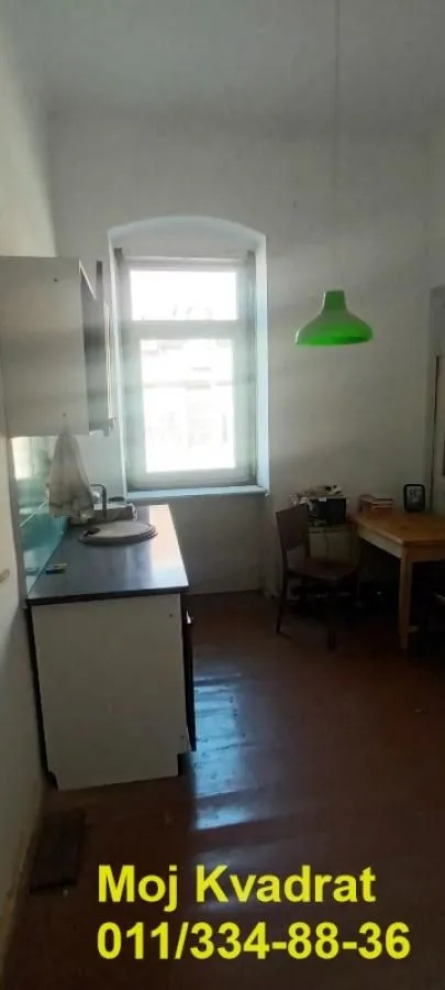 Manja kuhinja sa sudoperom, radnim elementima i trpezarijskim stolom pored prozora.