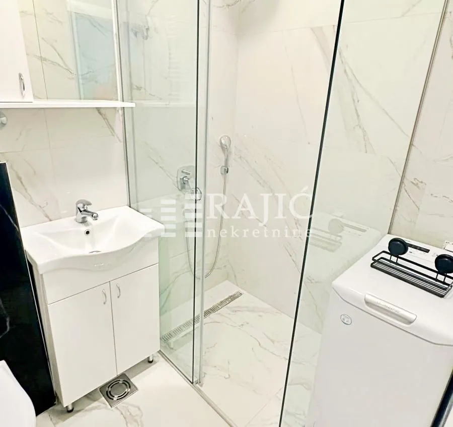 Modern bathroom with a sink, shower cabin, and washing machine.
