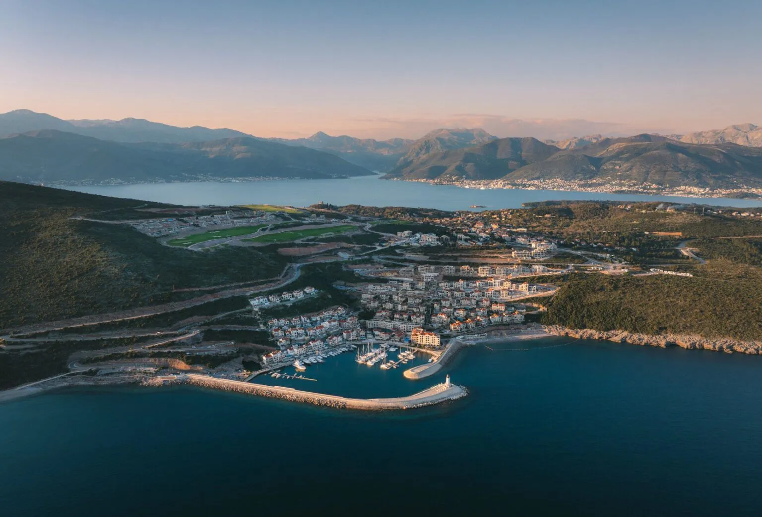 Pogled iz vazduha na priobalno naselje i marinu sa planinama u pozadini.