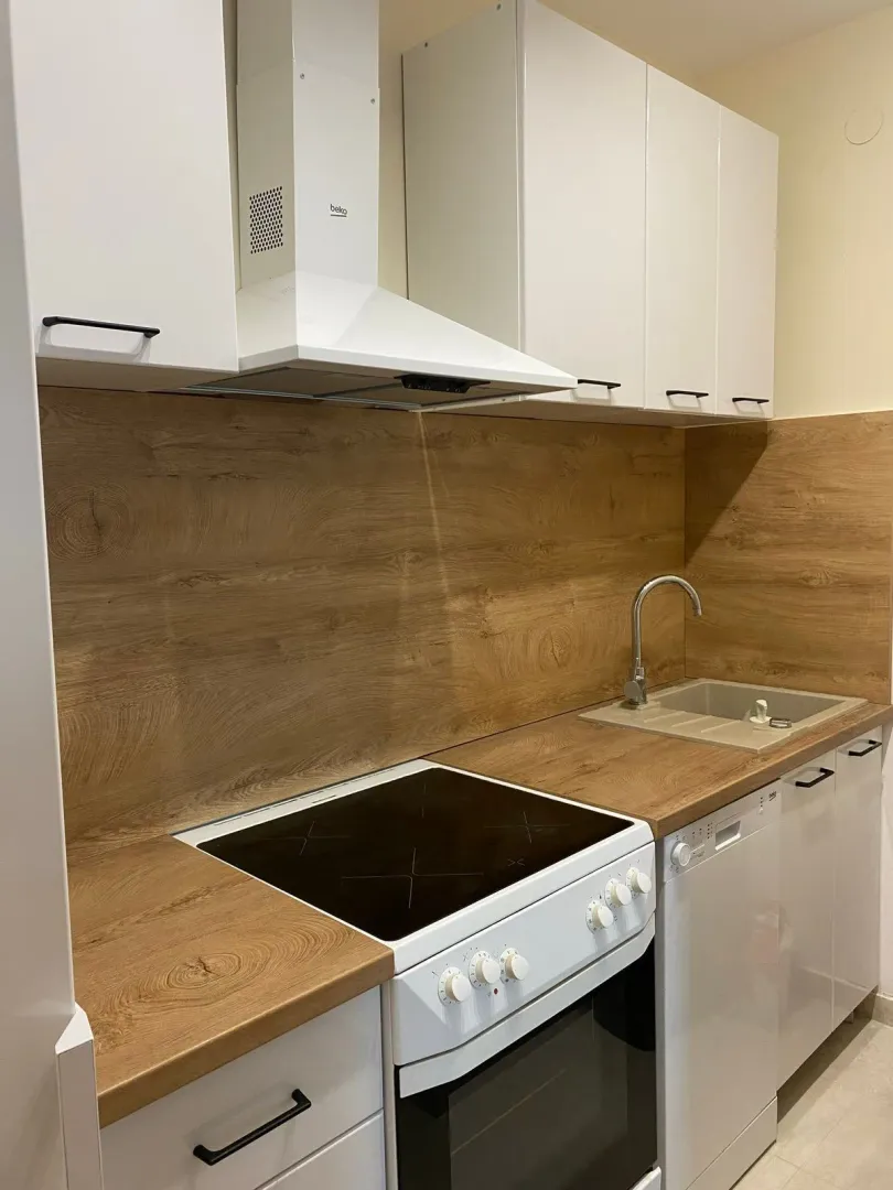 Compact kitchen with white cabinets, wooden countertop, and a stove.