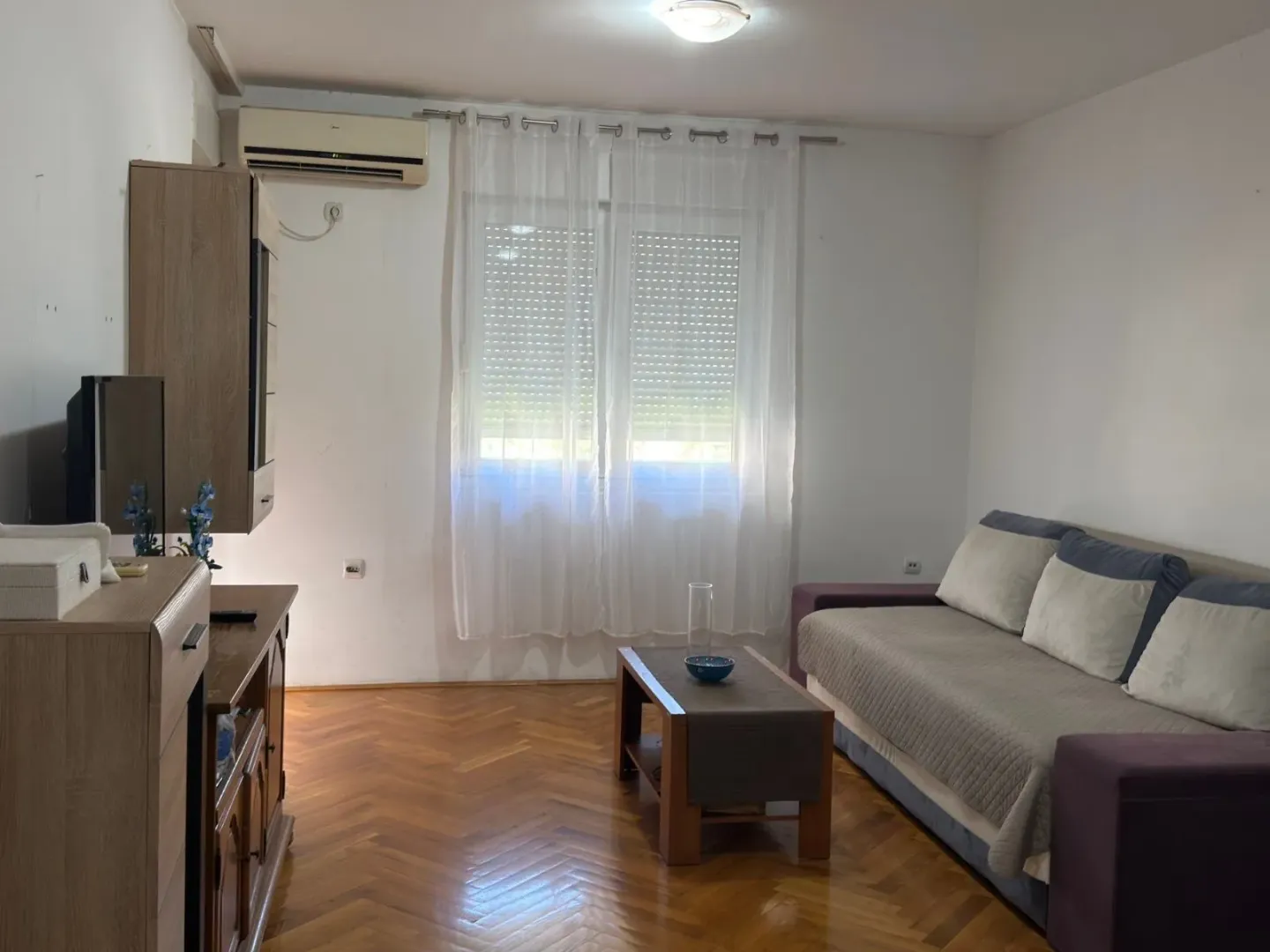 Dnevna soba sa garniturom za sedenje, televizorom i drvenim podom.