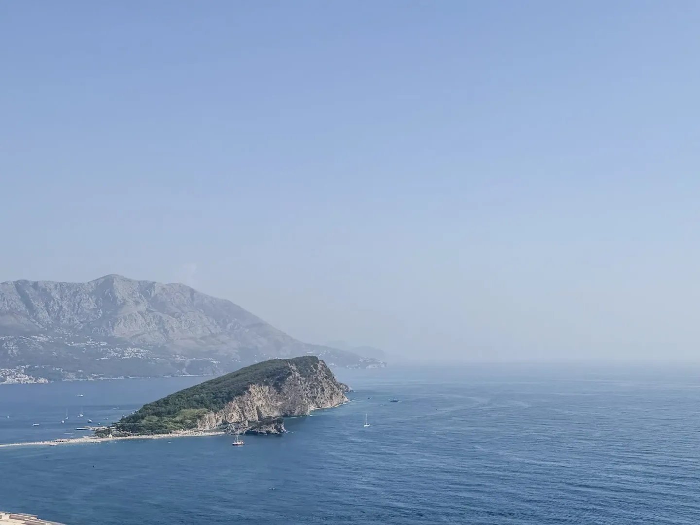 Pogled na more sa ostrvom i planinama u pozadini.