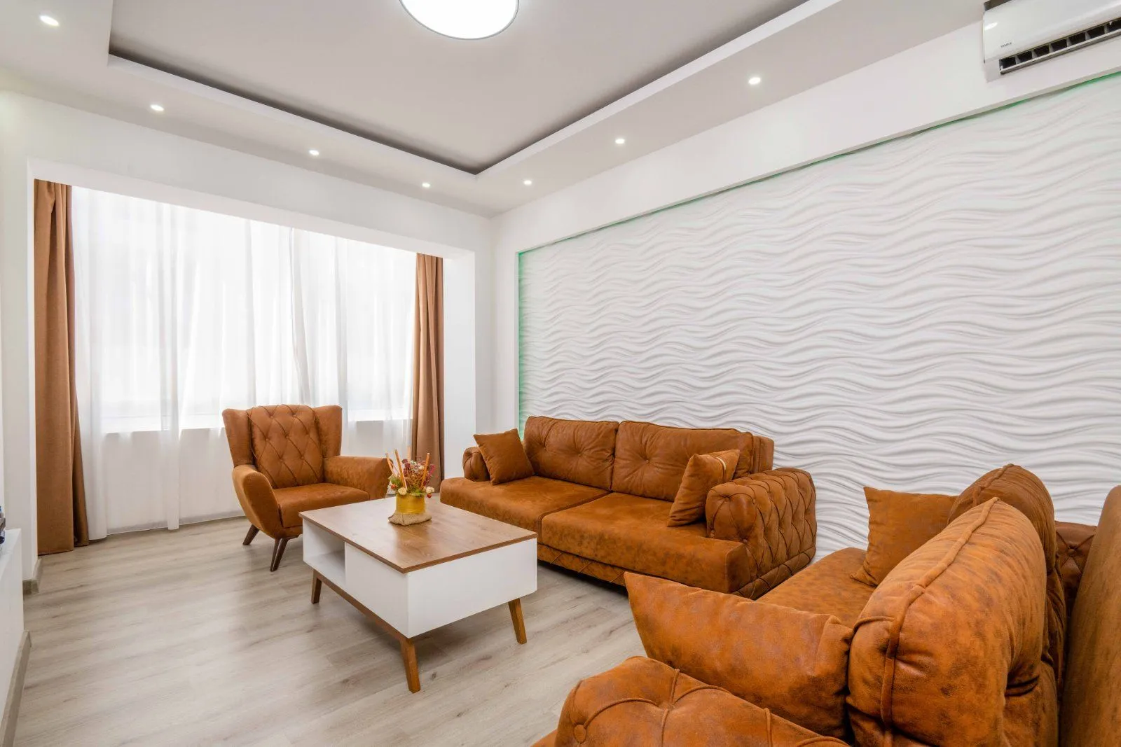 Living room with brown sofas, an armchair, a coffee table, and a decorative wall.