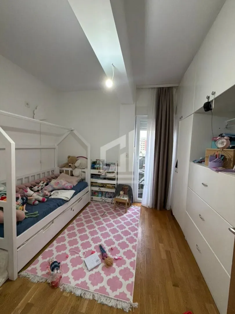 Dječja spavaća soba sa krevetom, bijelim ormarima i roze tepihom.