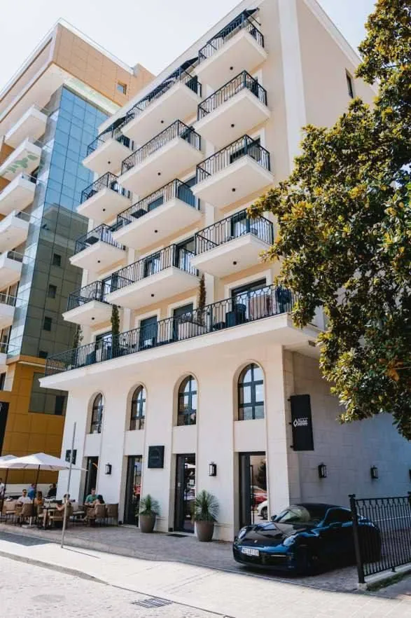 Exterior of a multi-story residential building with balconies and a car in the yard.