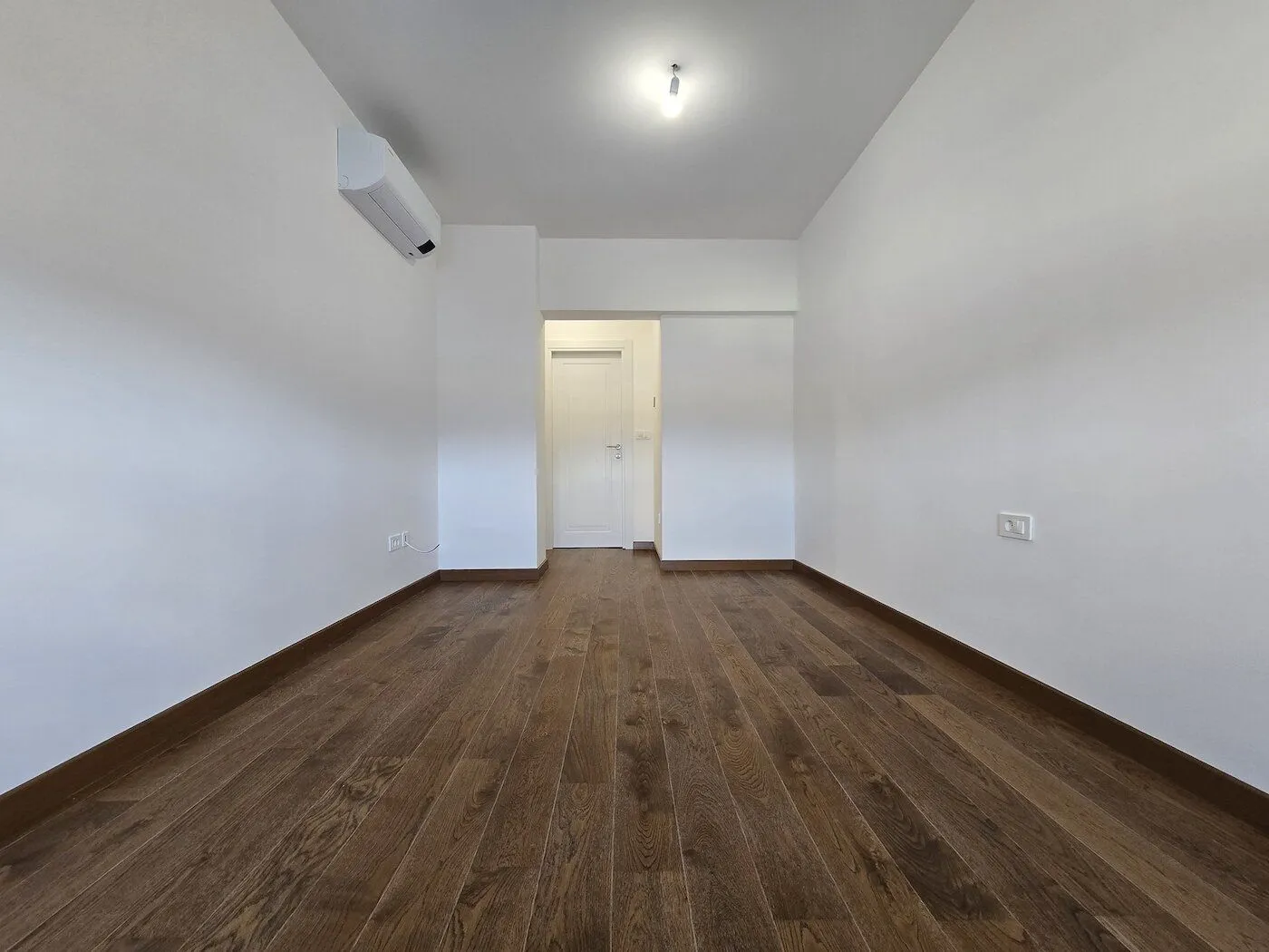 Empty room with white walls and wooden flooring.