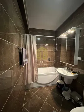 Manje kupatilo sa tuš kadom i umivaonikom obloženo smeđim pločicama. - image 10