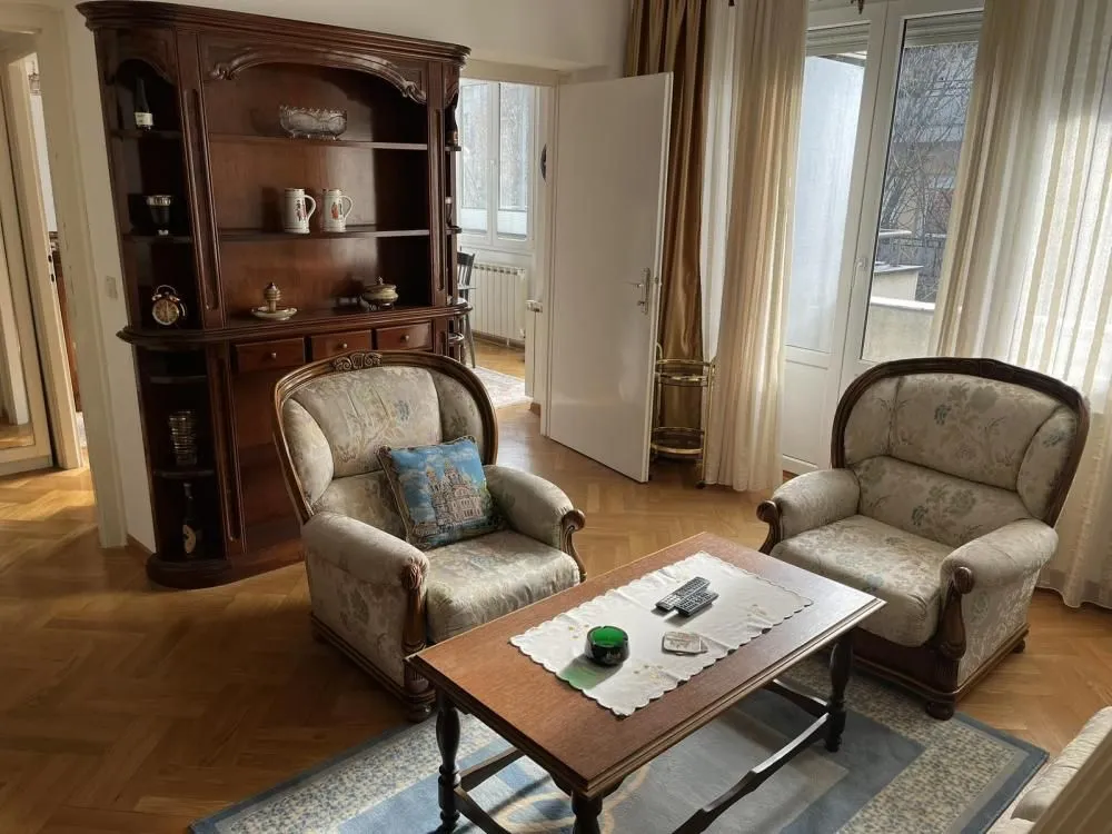 Living room with a seating arrangement, wooden display cabinet and parquet flooring.
