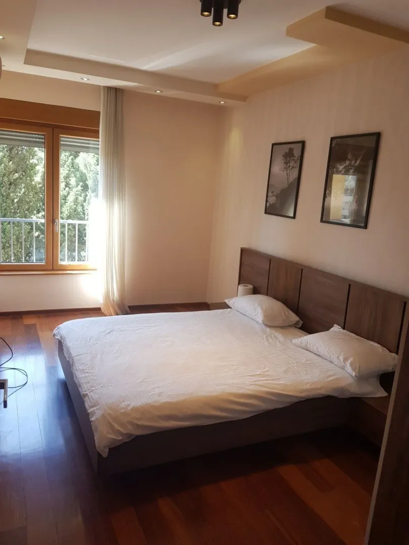 Bright bedroom with a double bed, wooden floors, and a large window.