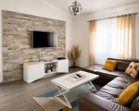 Decorated living room with a sectional sofa, wall-mounted TV on a decorative stone wall, and a coffee table. - image 14