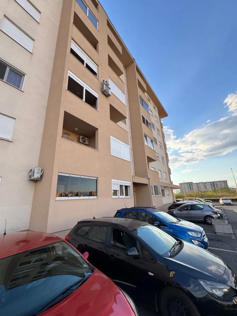 Pogled na spoljašnost stambene zgrade i parking ispred.