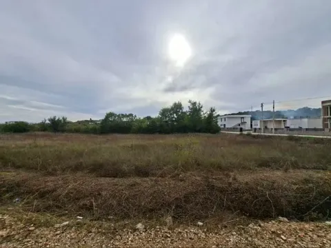 Pogled na prostrano zemljište sa rastinjem i okolnim kućama u pozadini. - image 3