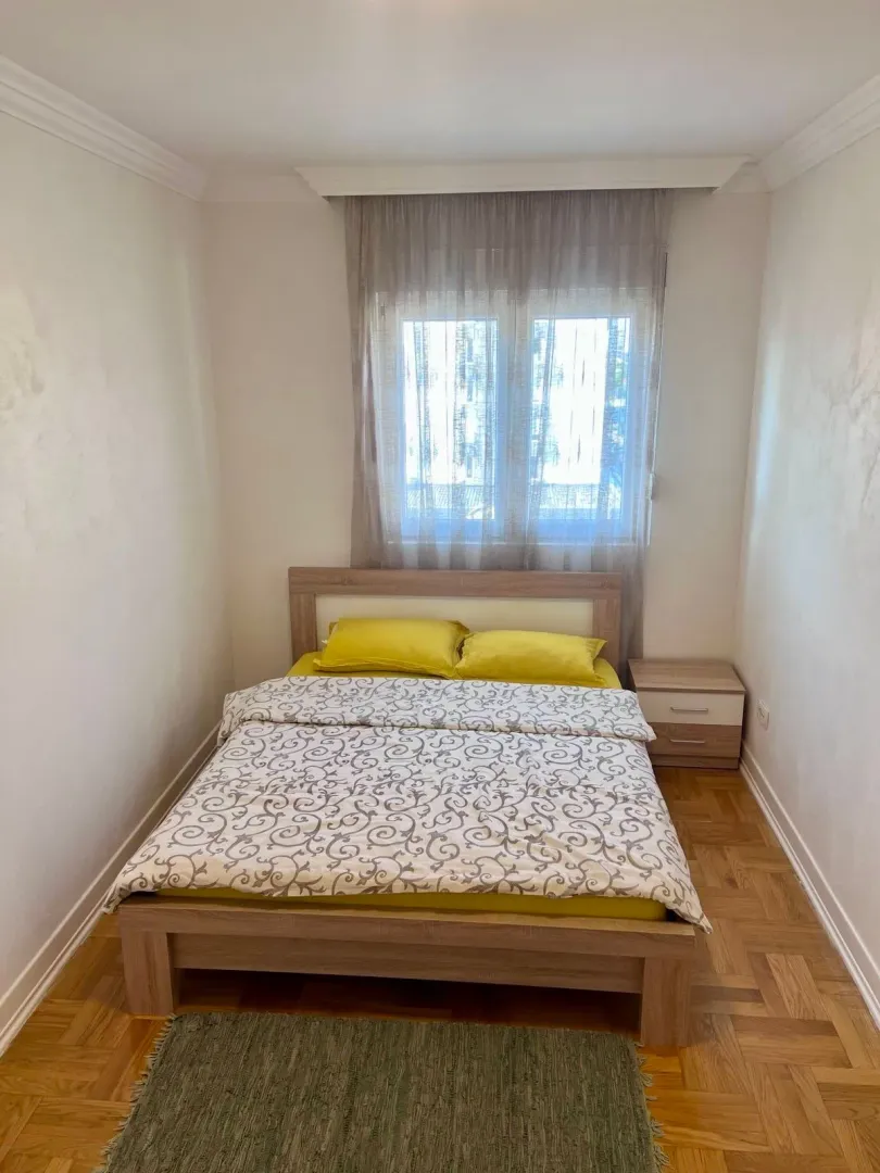 Spavaća soba sa bračnim krevetom, noćnim stočićem i prozorom.