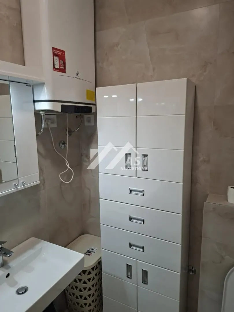 Kupatilo sa umivaonikom, bojlerom i belim ormarićem za odlaganje.