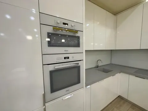 Modern white kitchen with built-in ovens and a gray countertop. - image 10