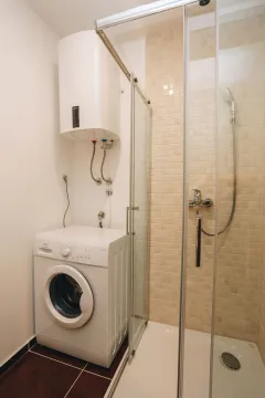 Small bathroom with a shower cabin, water heater, and washing machine. - image 14