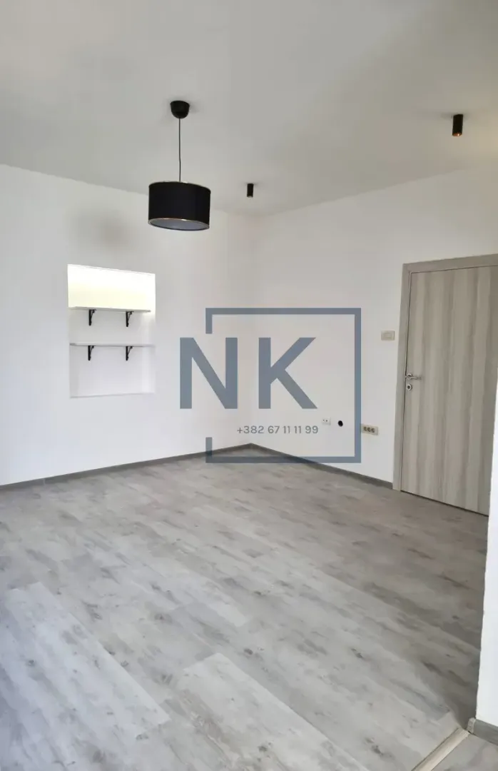 Empty room with white walls, laminate flooring, pendant light, and a door.