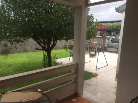 View from a covered terrace overlooking a paved yard with a lawn and a children's swing. - image 9