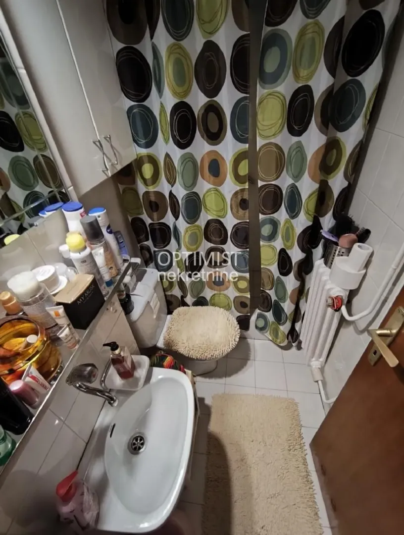 Manje kupatilo sa umivaonikom, WC šoljom i tuš kabinom sa zavesom.