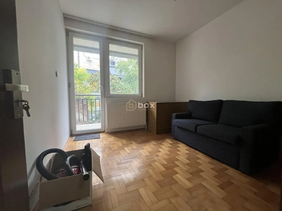 Smaller room with parquet flooring, a dark sofa, and access to the terrace.