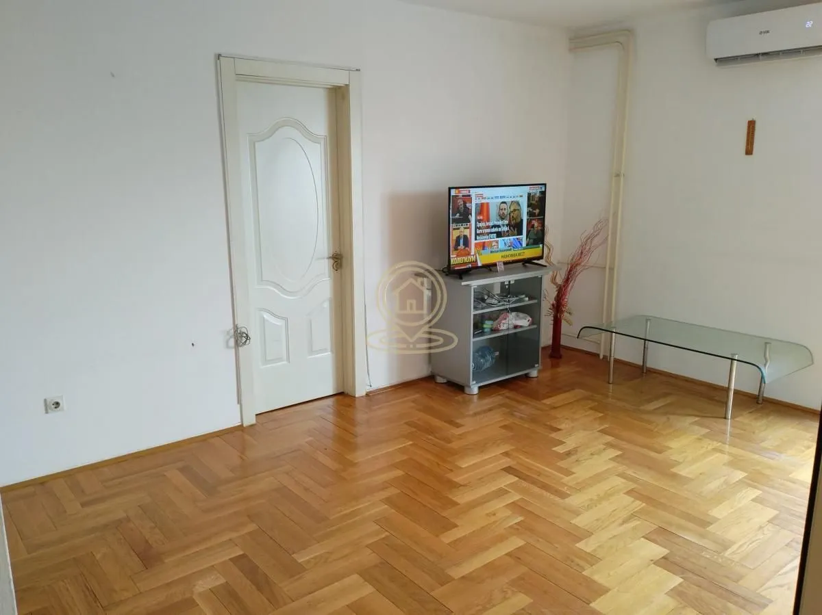 Dnevna soba sa drvenim parketom, televizorom na komodi i klima uređajem.