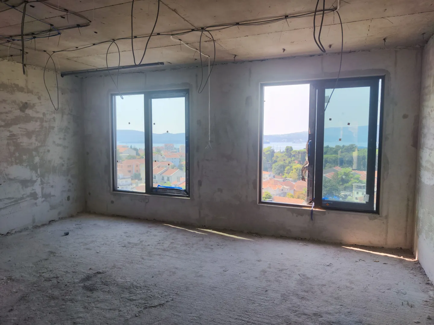 Nenameštena prostorija u sivoj fazi sa dva prozora i pogledom na grad.
