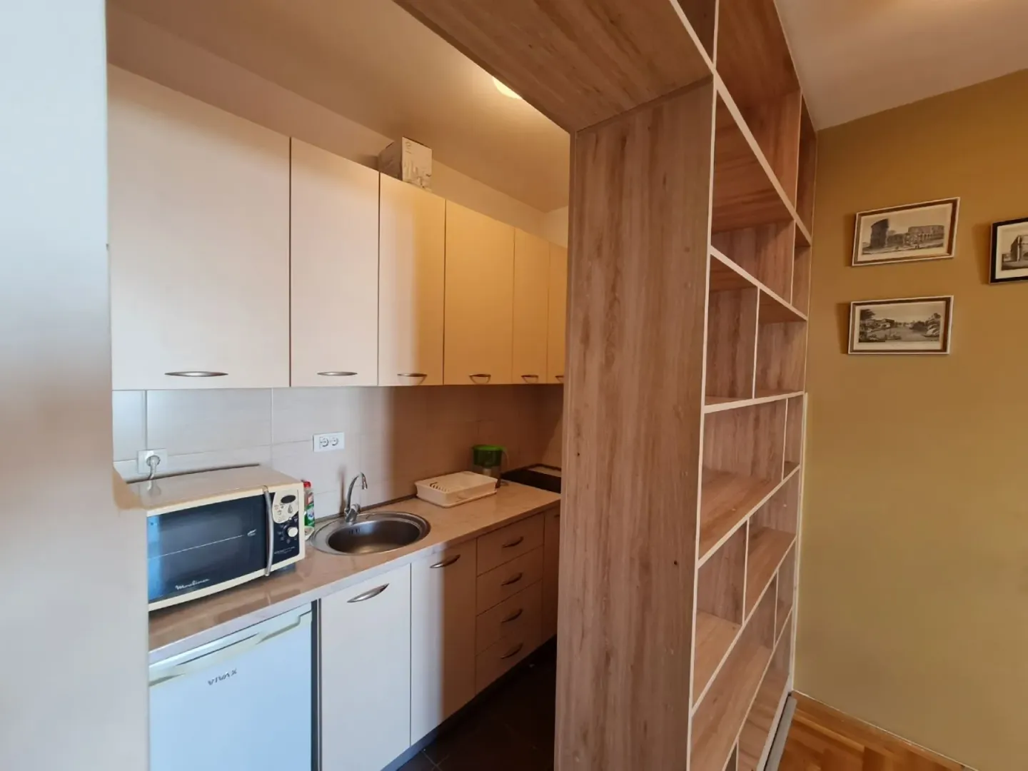 A small kitchen with light cabinets and a wooden room divider shelf.