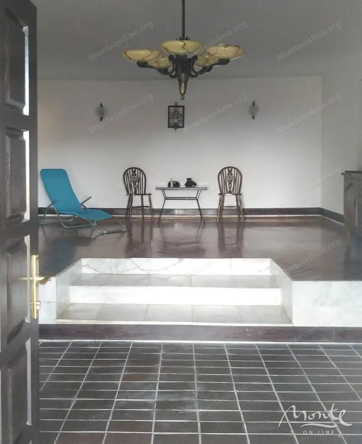 Spacious living room with wooden flooring, marble steps, and a chandelier.