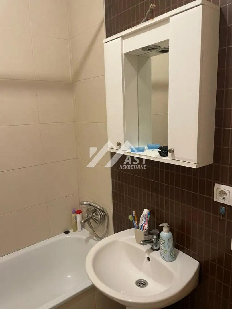 Manje kupatilo sa kadom, umivaonikom i ormarićem sa ogledalom.