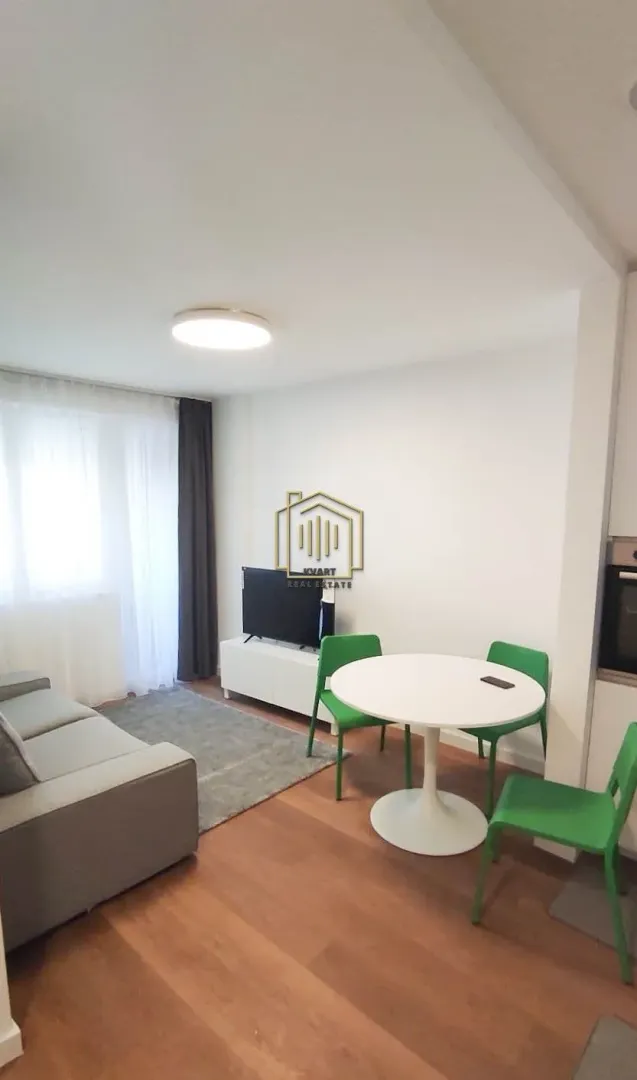 Dnevni boravak sa garniturom, TV-om i trpezarijskim stolom sa zelenim stolicama.