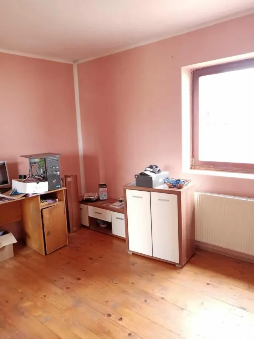 Prazna soba sa roze zidovima, drvenim podom, radnim stolom i prozorom.