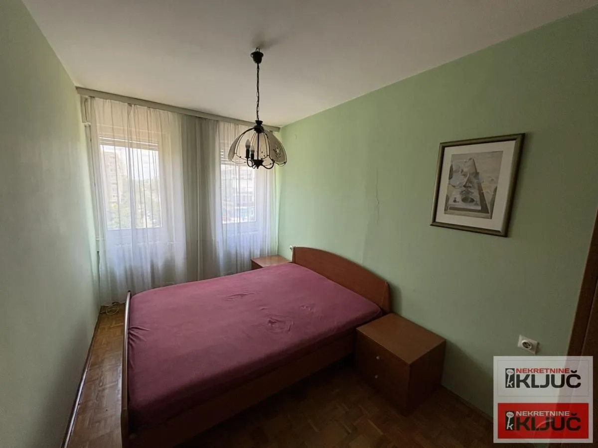 Spavaća soba sa bračnim krevetom, noćnim stočićima i prozorom sa zavesama.