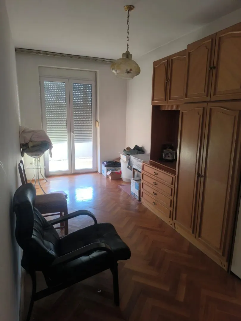 Manja soba sa drvenim garderoberom, foteljom i izlazom na terasu.