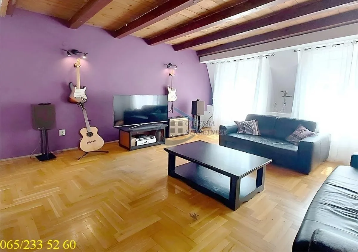 Living room with sofa, TV, wooden ceiling beams and a purple wall.
