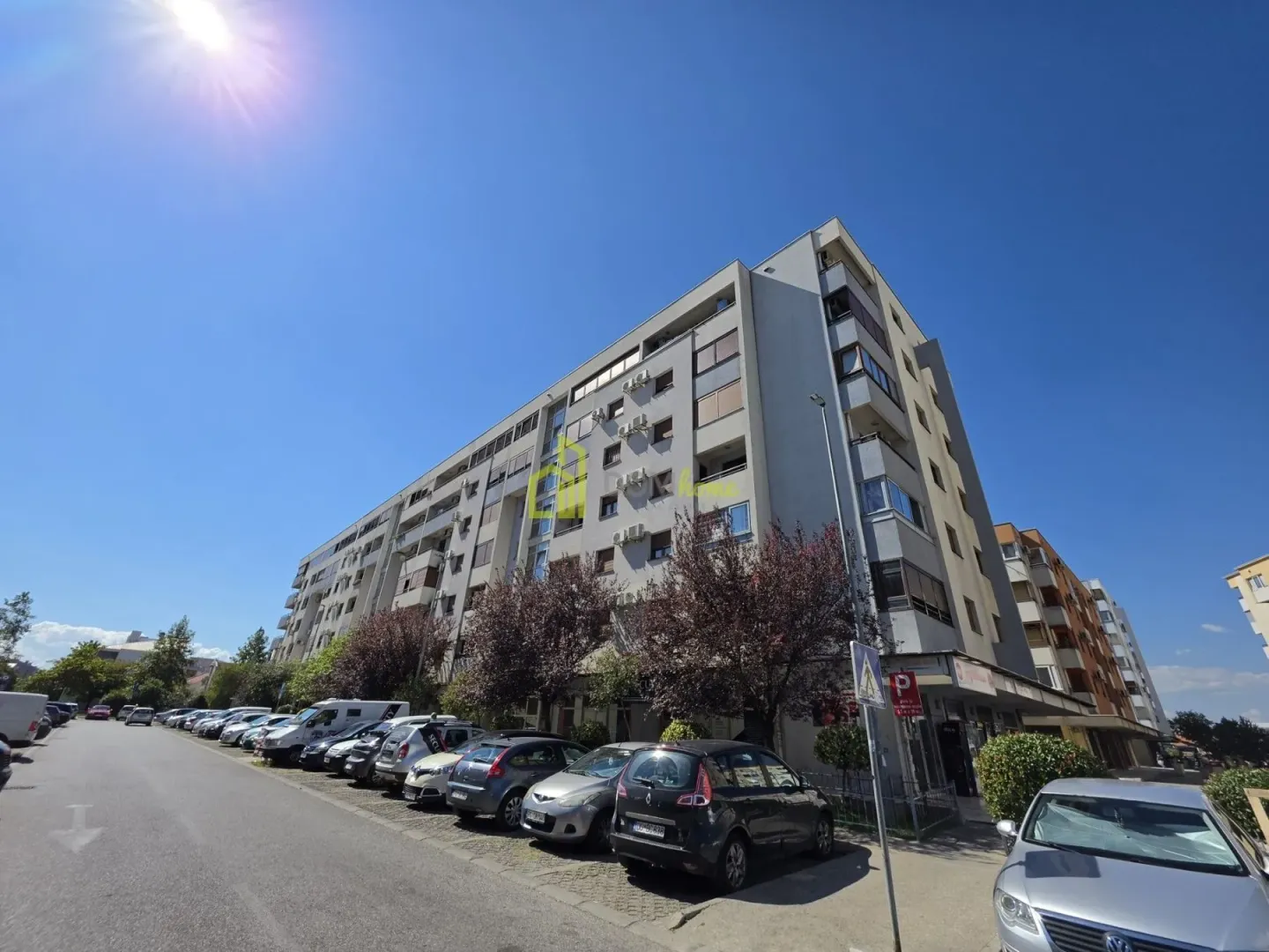 Pogled na spoljašnjost stambene zgrade i parking sa parkiranim automobilima.