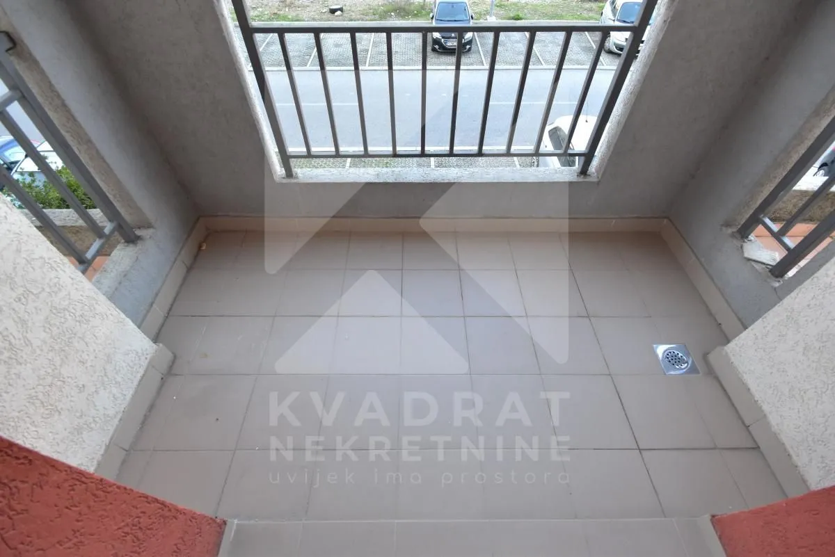 Pogled na nenamješten balkon sa metalnom ogradom i keramičkim pločicama.