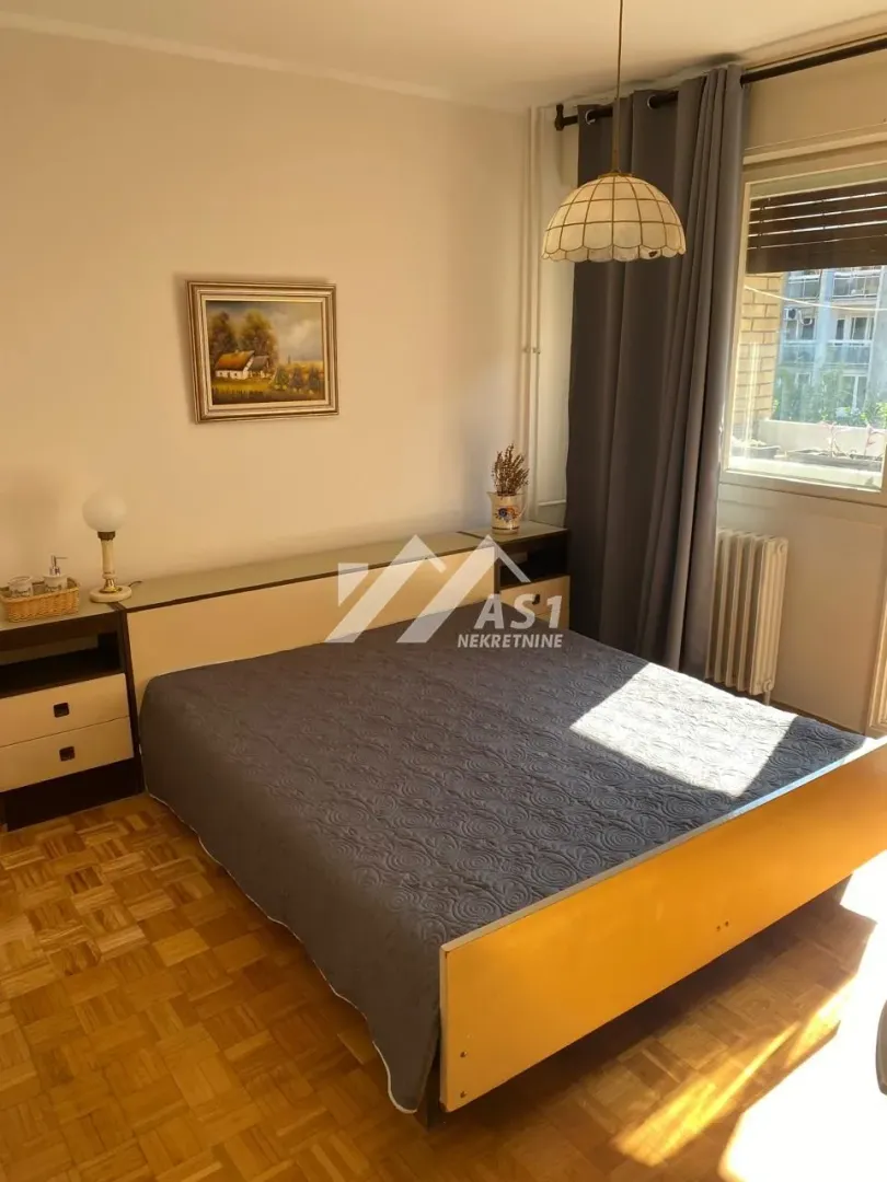 Nameštena spavaća soba sa bračnim krevetom, noćnim stočićima i prozorom.