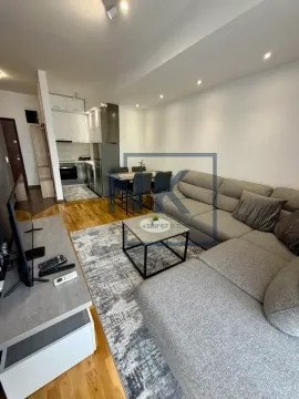 Living room with a sofa, TV stand, dining area, and kitchen in the background. - image 2