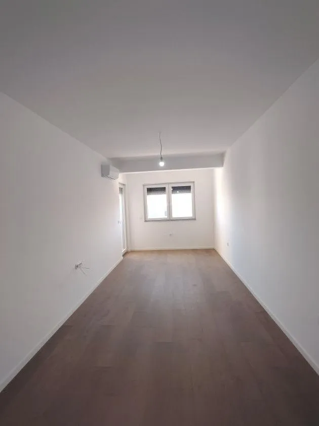 Prazna soba sa bijelim zidovima i drvenim podom.