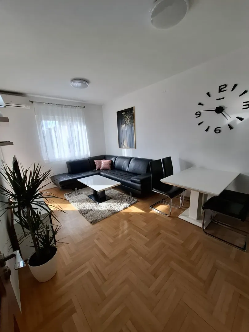 Bright living room with a black leather sofa and a dining table.