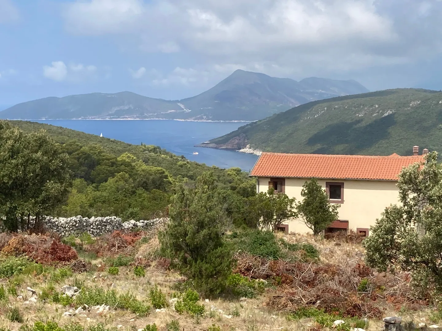 Pogled na kuću sa krovom od crijepa i okolni pejzaž sa morem u pozadini.