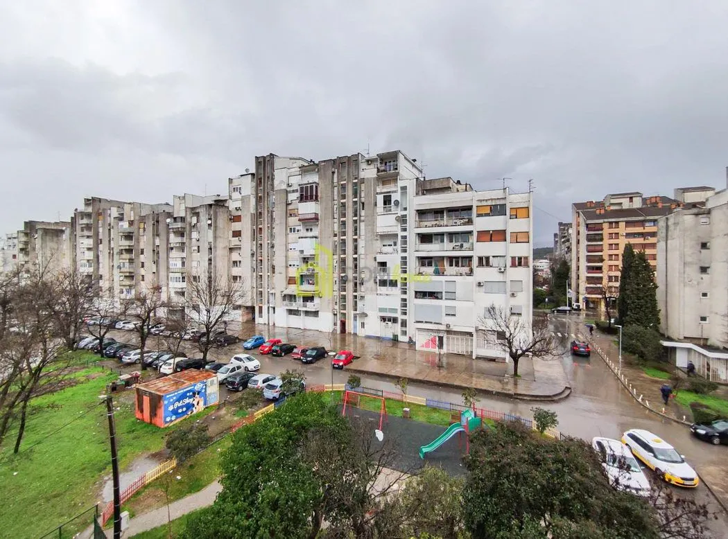 Pogled sa prozora na okolne zgrade, parking i zelenu površinu.